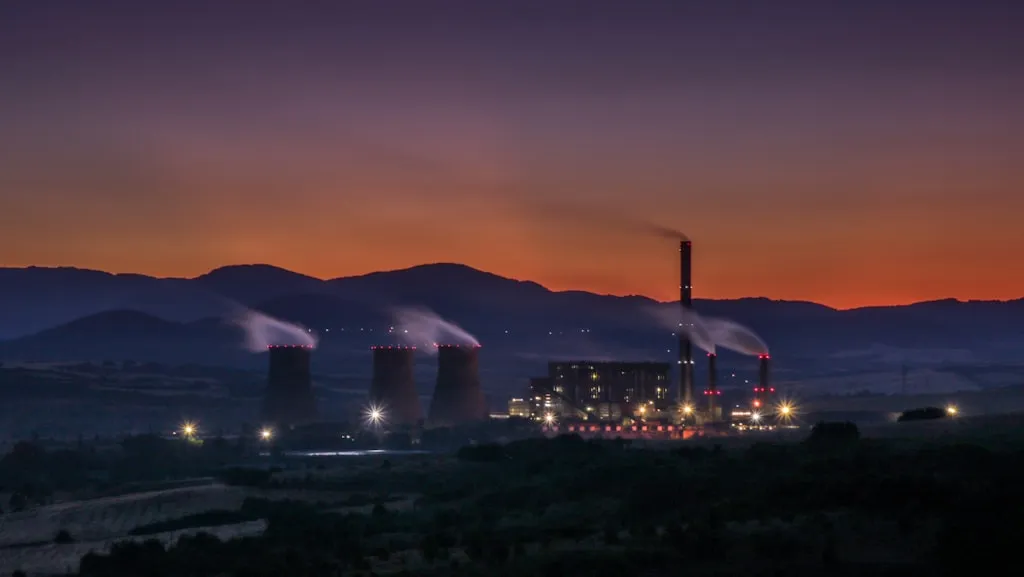 夕暮れのオレンジ色の空を背景にシルエットで浮かぶ火力発電所の煙突と冷却塔