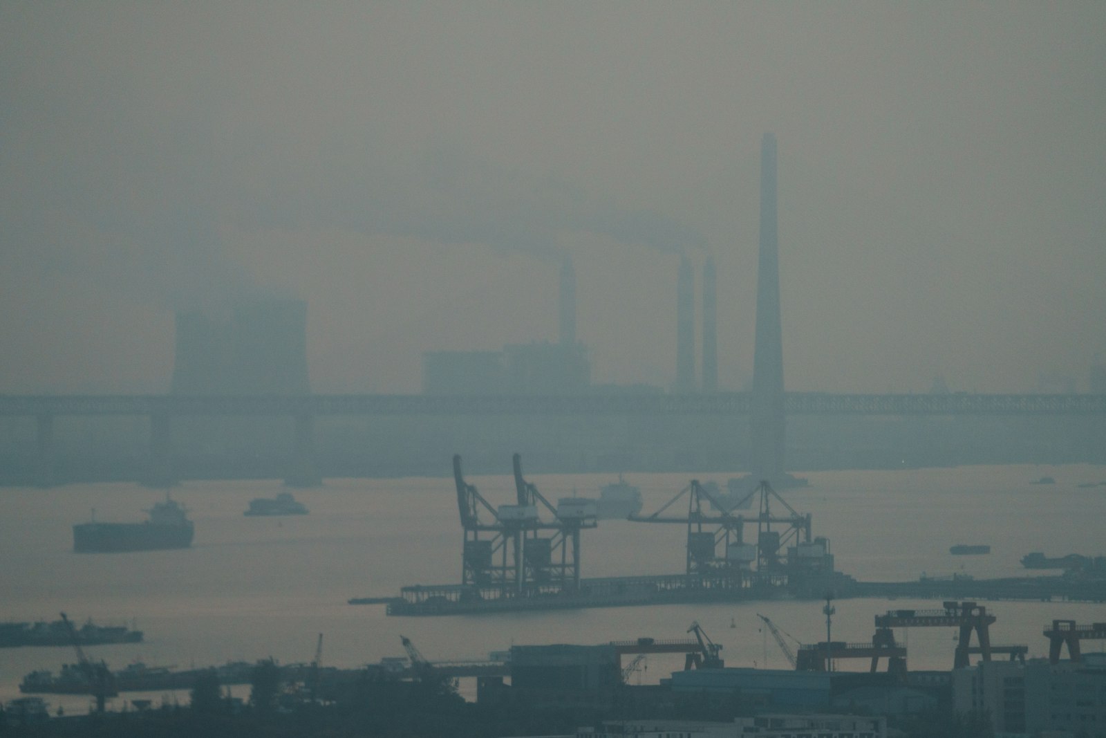 霧の中にクレーンと煙突が立ち並ぶ工業港湾の遠景